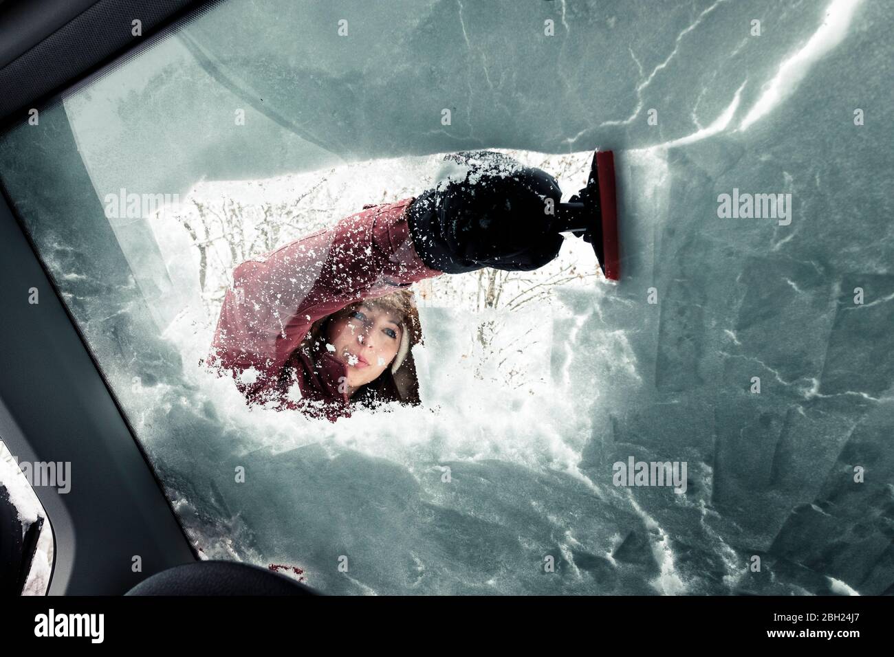 Porträt einer jungen Frau, die Schnee von der Windschutzscheibe des Autos putzt Stockfoto