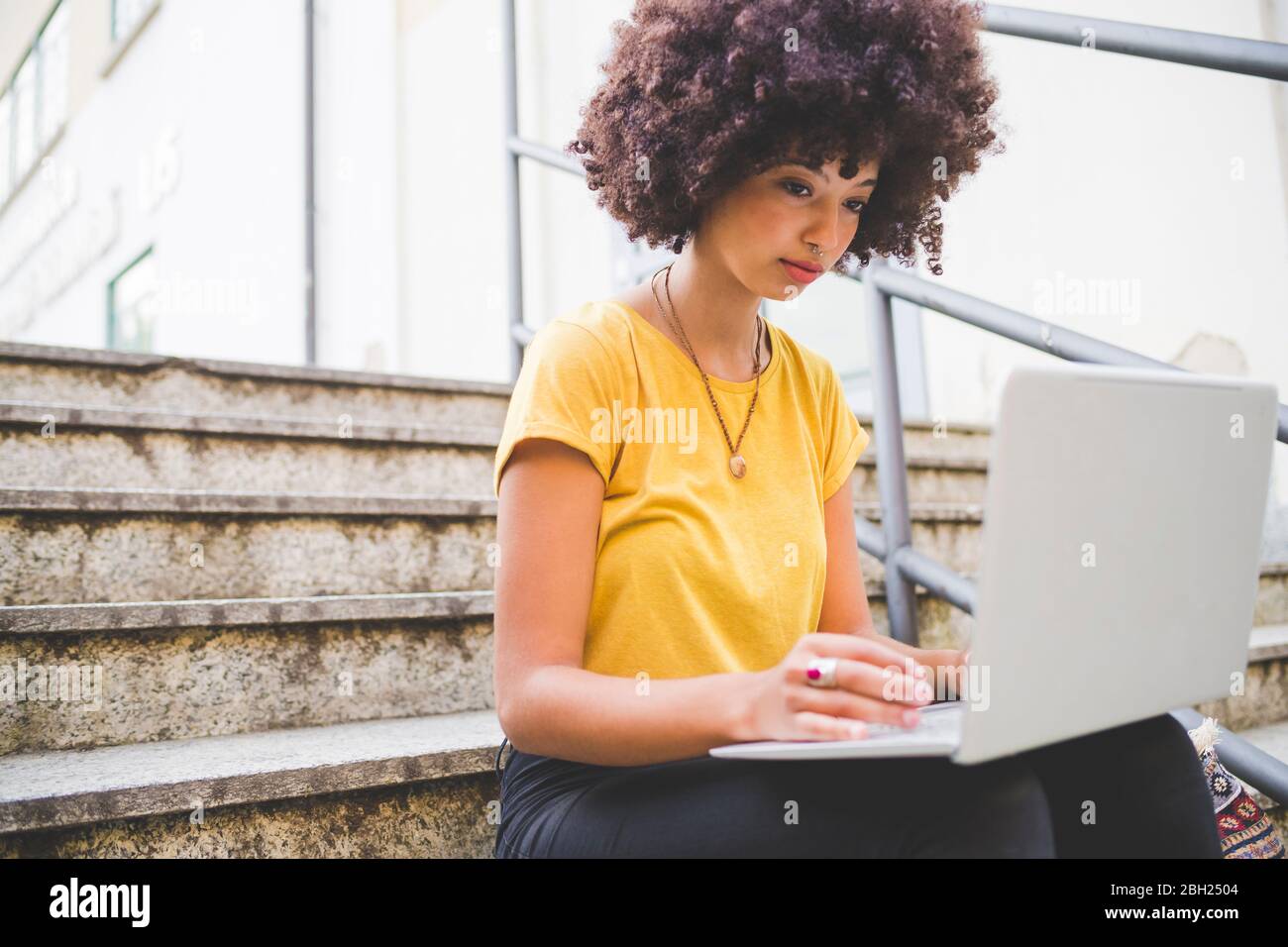 Junge Frau mit Afro-Frisur mit Laptop auf Treppen in der Stadt Stockfoto