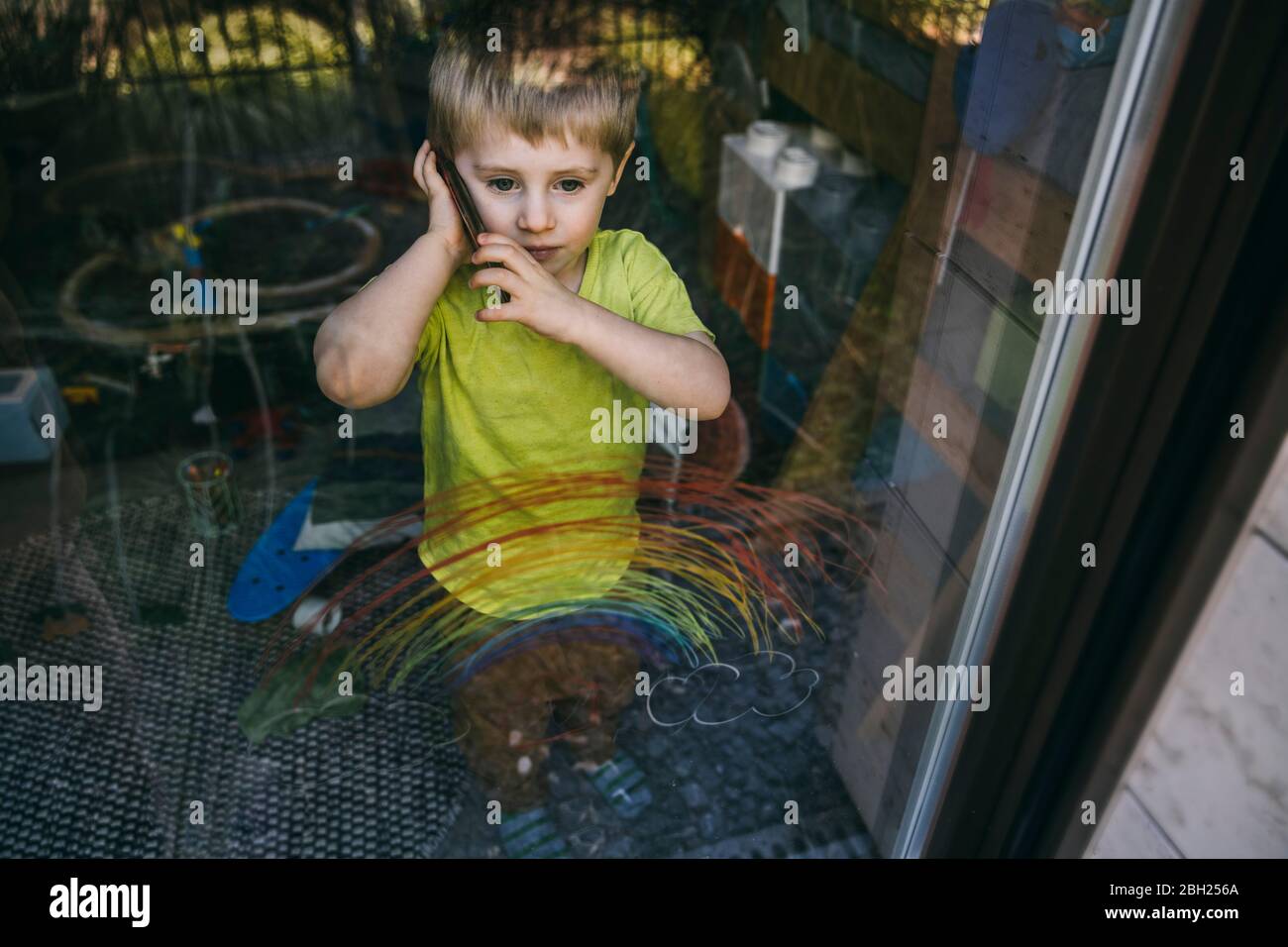 Porträt eines kleinen Jungen am Telefon hinter Balkontür stehend Stockfoto