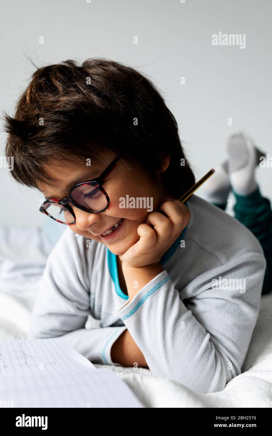 Portrait eines kleinen Jungen auf dem Bett liegend bei Hausaufgaben Stockfoto