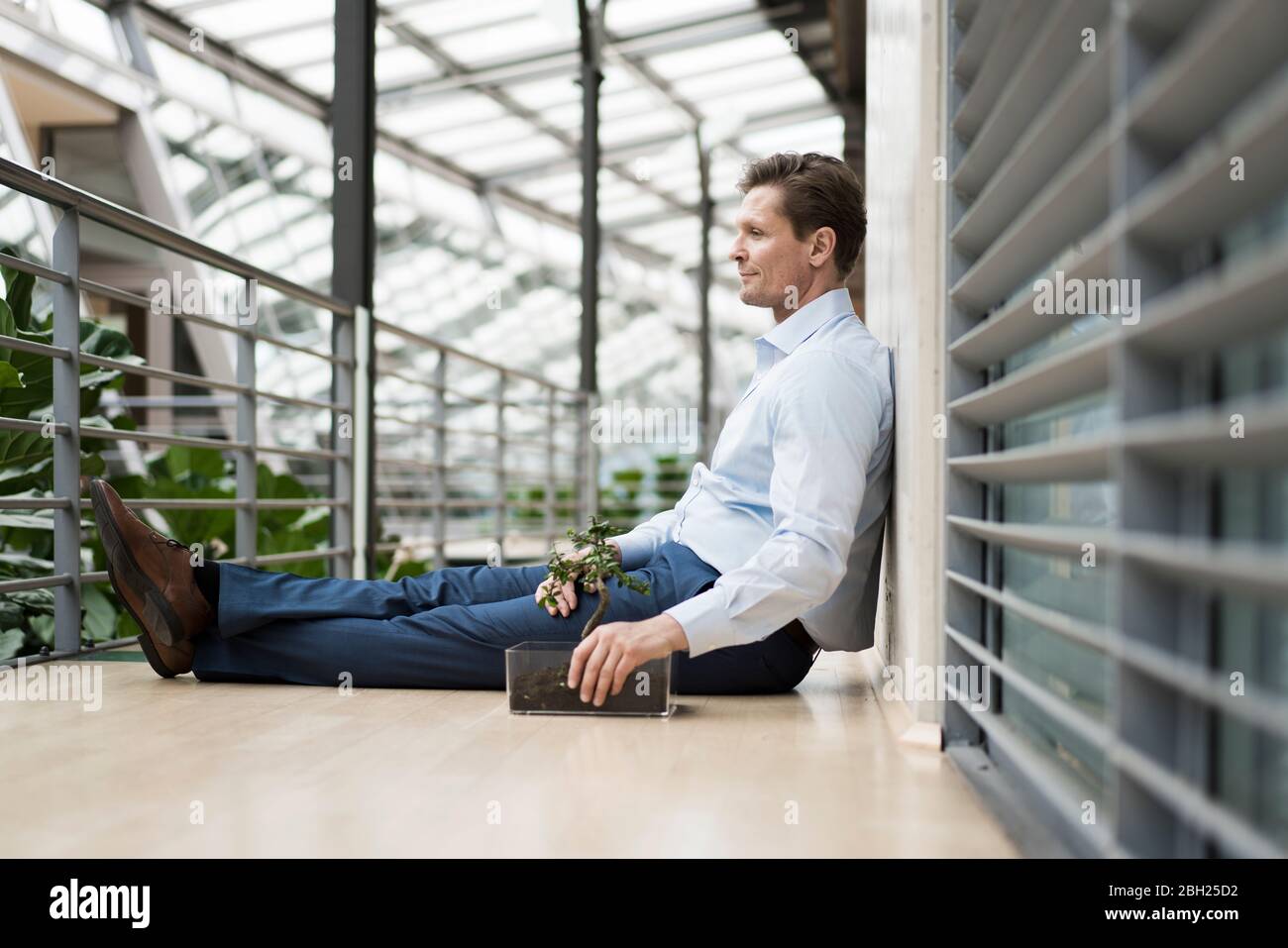 Geschäftsmann im grünen Atrium, auf der Galerie sitzend Stockfoto