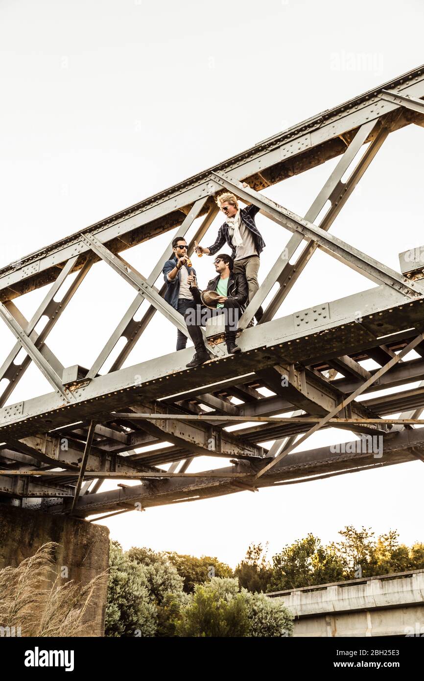 Drei Männer trinken Bier auf einer alten Eisenbahnbrücke Stockfoto