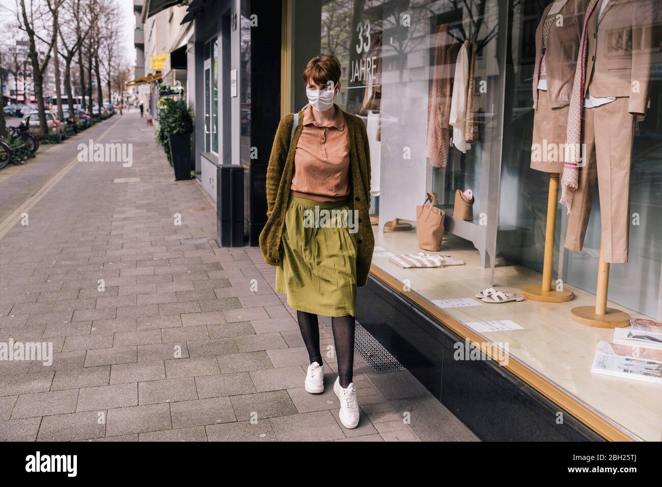 Frau trägt Maske zu Fuß entlang Bekleidungsgeschäft in der Stadt Stockfoto