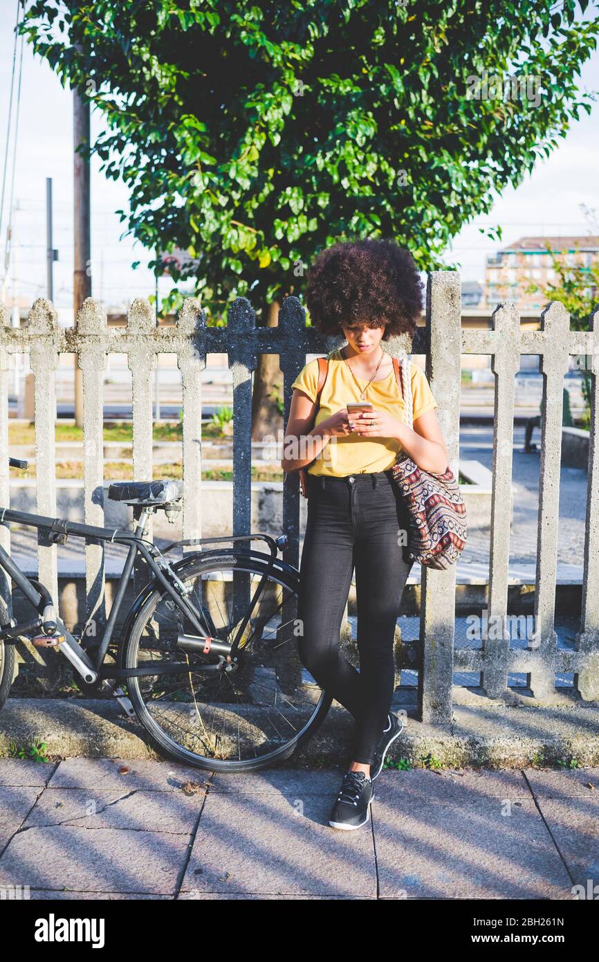 Junge Frau mit Afro-Frisur mit Smartphone in der Stadt Stockfoto