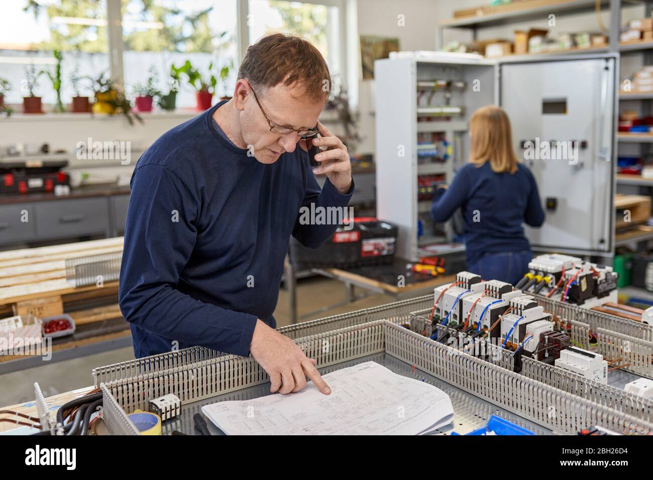 Mann am Telefon, Überprüfung des Schaltplans in der Elektrowerkstatt Stockfoto