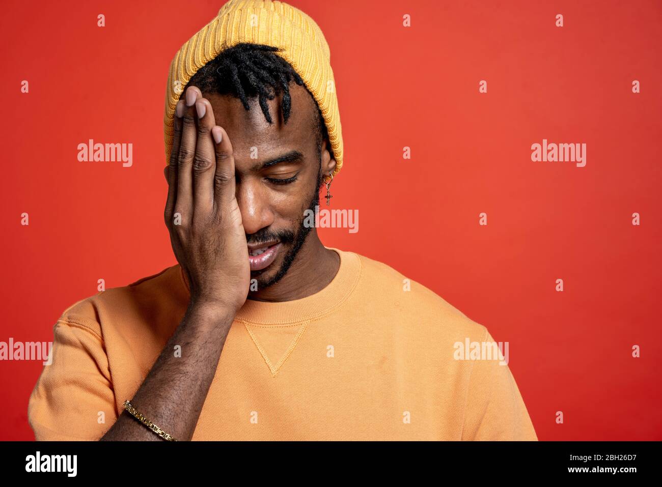 Porträt eines stilvollen jungen Mannes mit einem Auge vor der orangen Wand Stockfoto