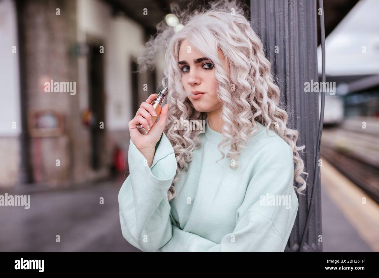 Portrait einer jungen Frau, die elektronische Zigarette auf der Plattform raucht Stockfoto