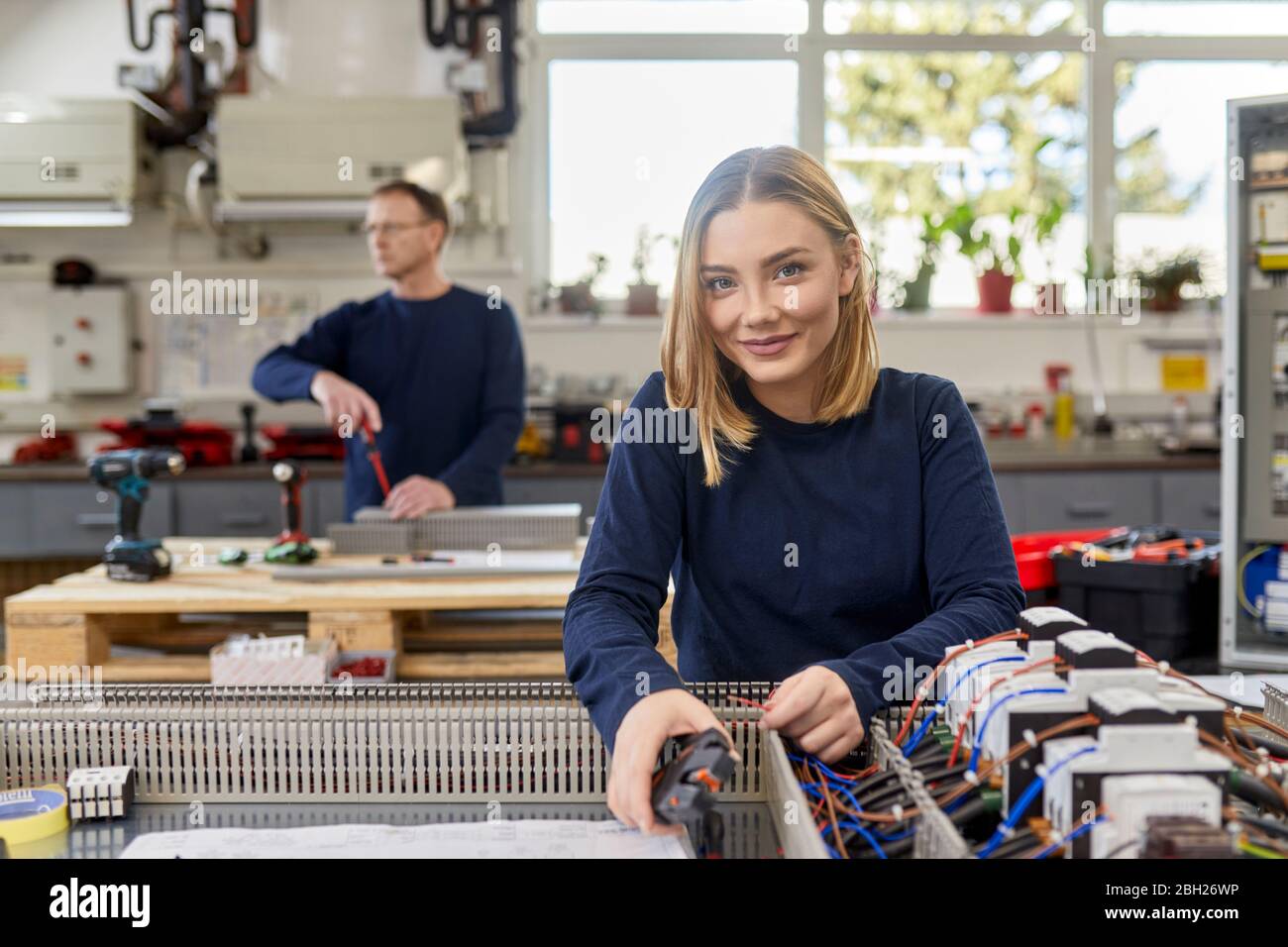 Portrait einer lächelnden Elektrikerin, die in der Werkstatt an Schaltkreisen arbeitet Stockfoto