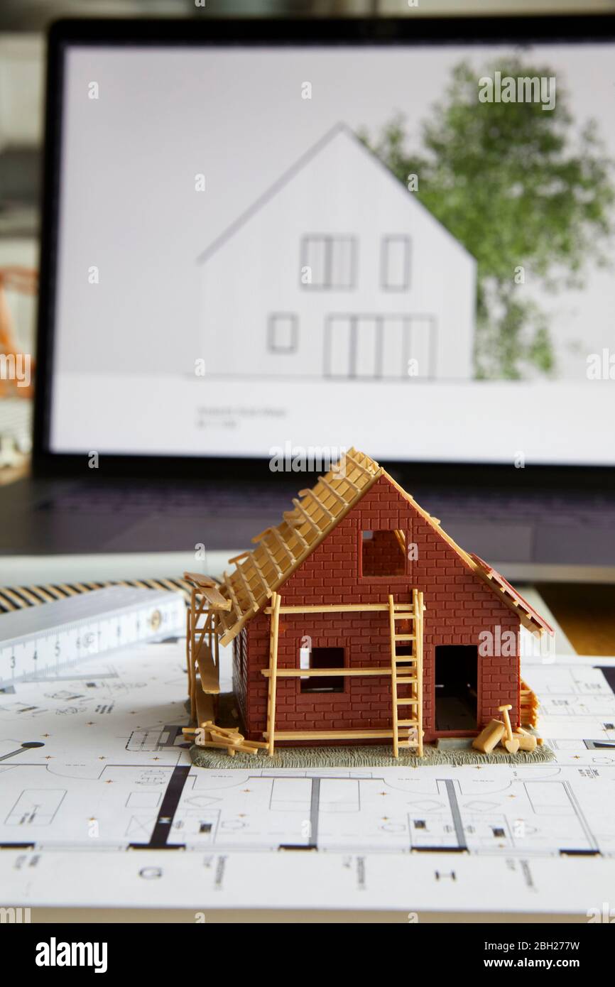 Architekturmodell des Eigenheims auf Bauplan, Laptop im Hintergrund Stockfoto