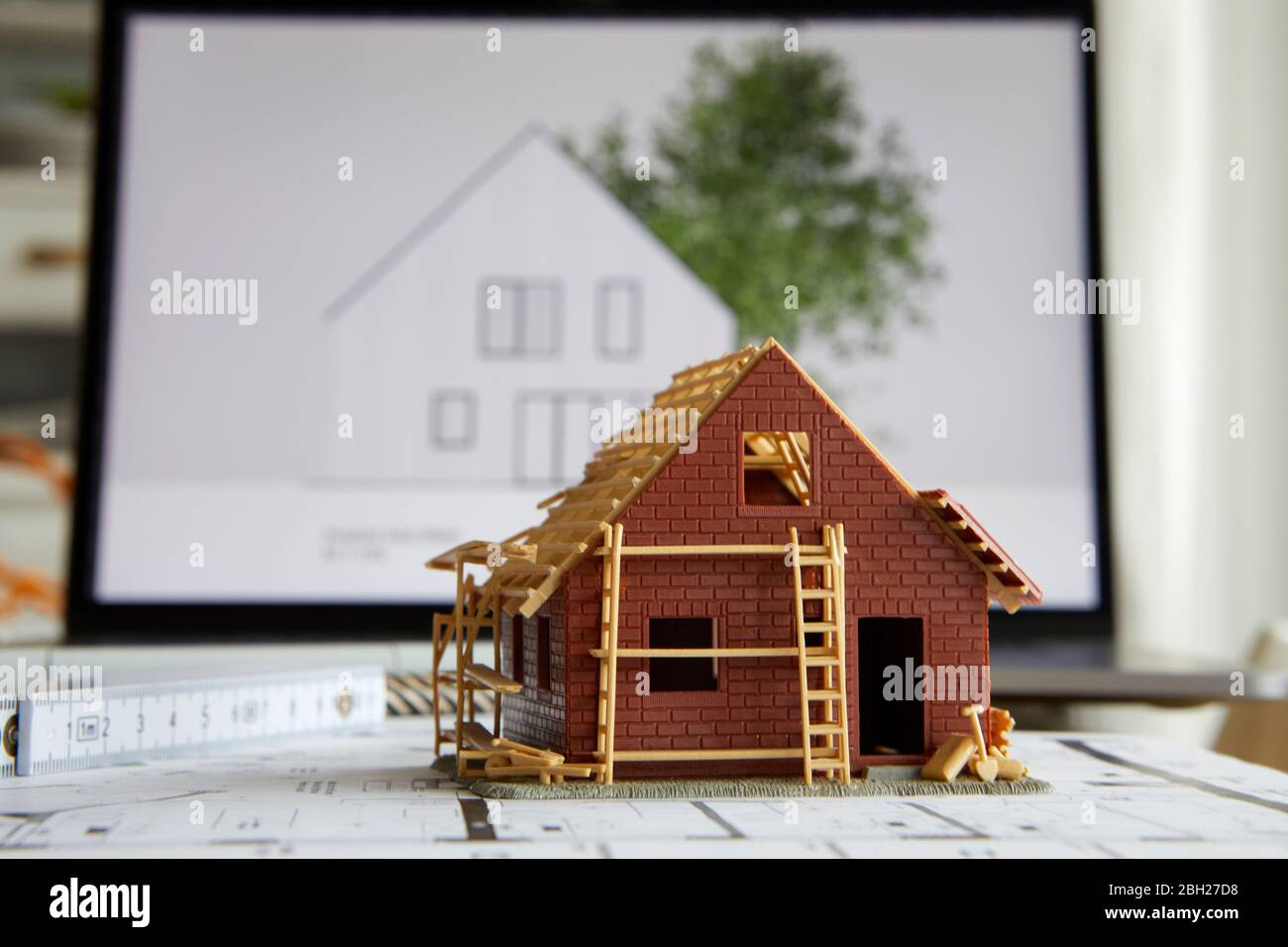 Architektur, Modell des Eigenheims auf Bauplan, Laptop im Hintergrund Stockfoto