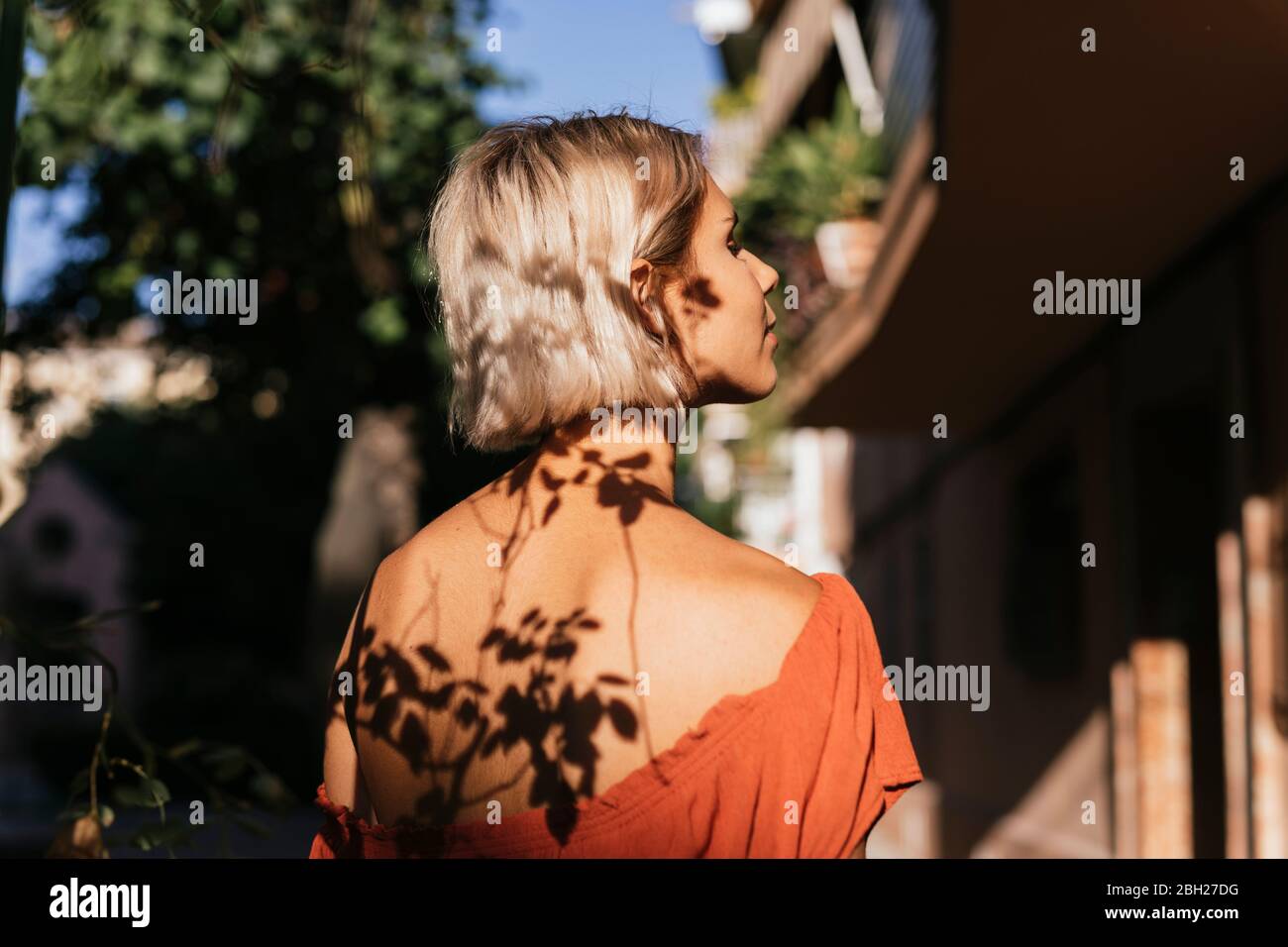 Junge Frau bei Sonnenlicht mit Schatten der Blätter auf Gesicht und Rücken Stockfoto
