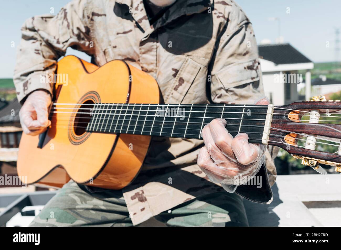 Soldat spielt Gitarre, mit Schutzhandschuhen Stockfoto