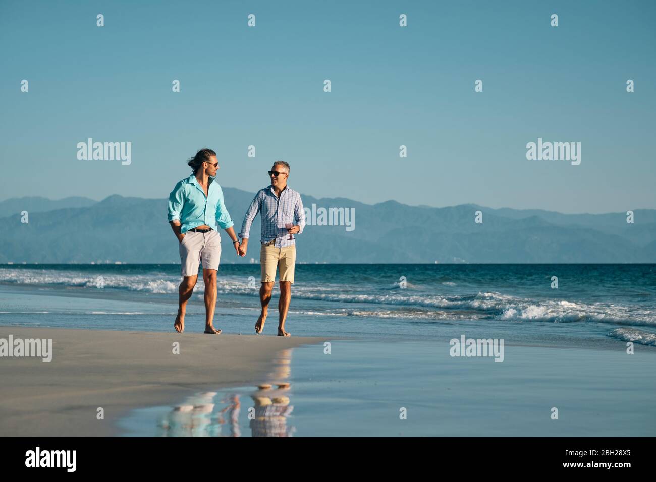 2 schwule Männer, die Hand in Hand an einem abgelegenen Strand in Mexiko gehen. Stockfoto