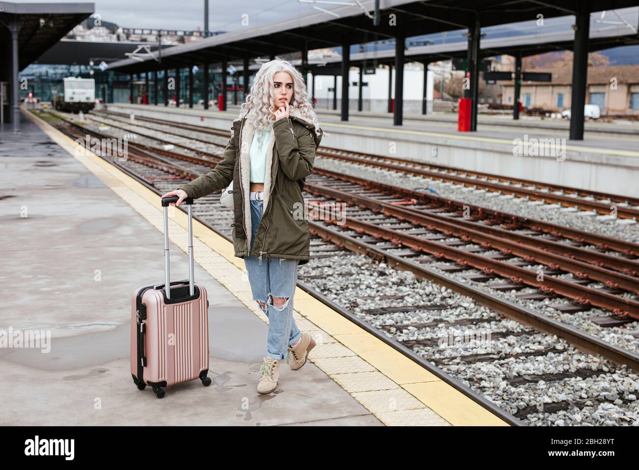 Porträt einer jungen Frau mit rollendem Koffer auf der Plattform Stockfoto