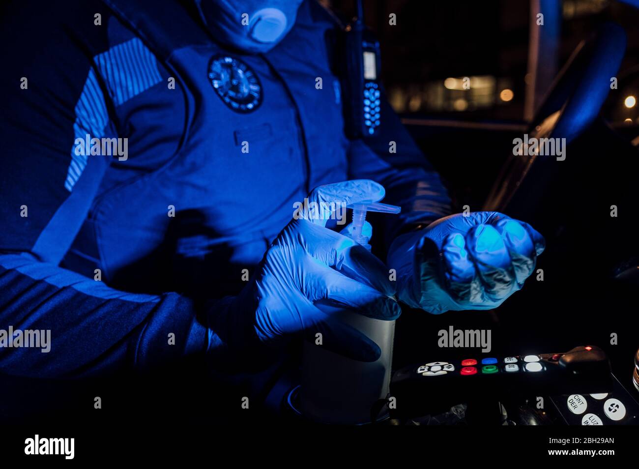 Polizist trägt Maske, Schutzhandschuhe und Desinfektionsmittel während der Notmission in der Nacht Stockfoto