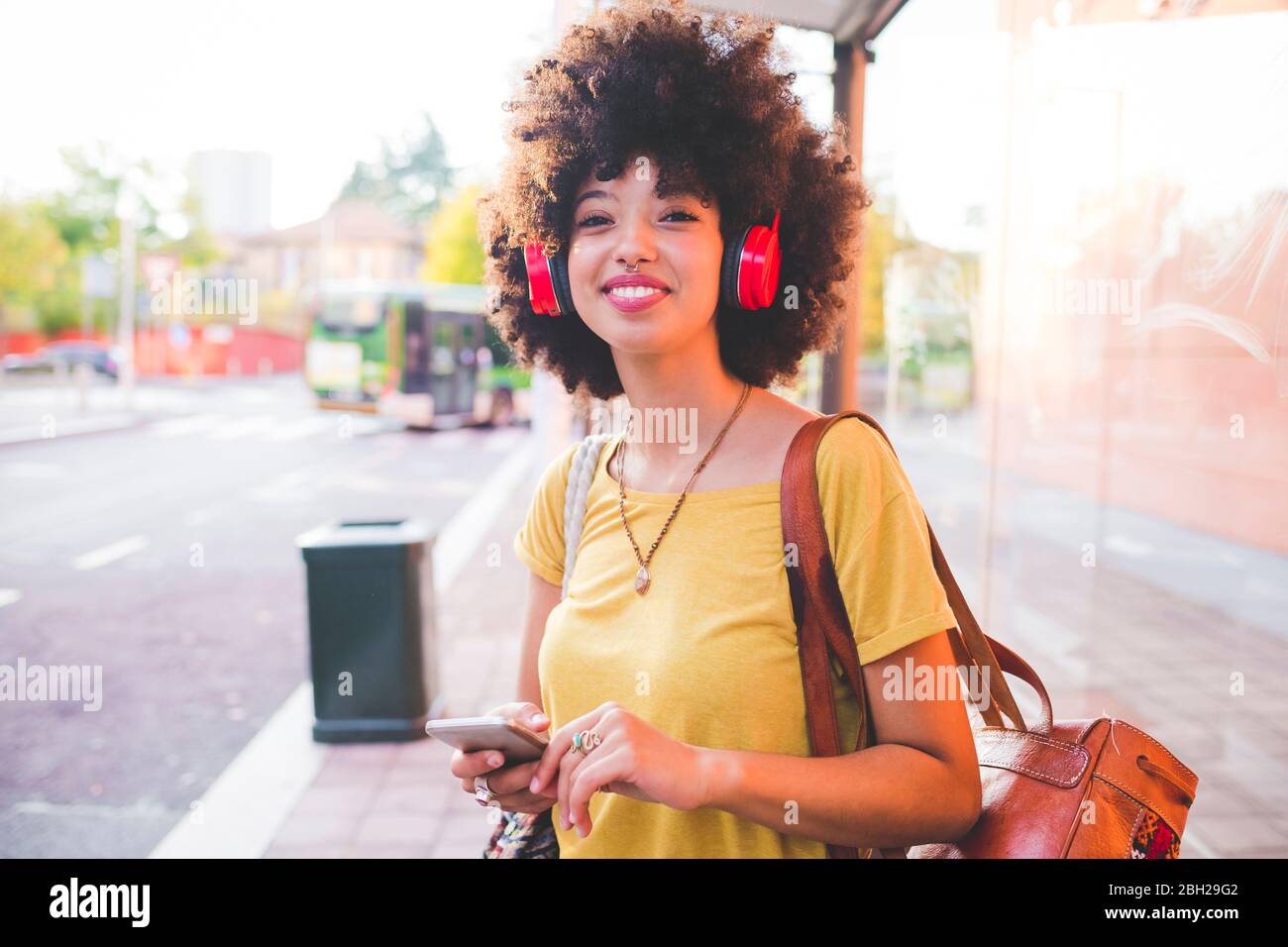 Glückliche junge Frau mit Afro-Frisur Musik mit Kopfhörern in der Stadt hören Stockfoto