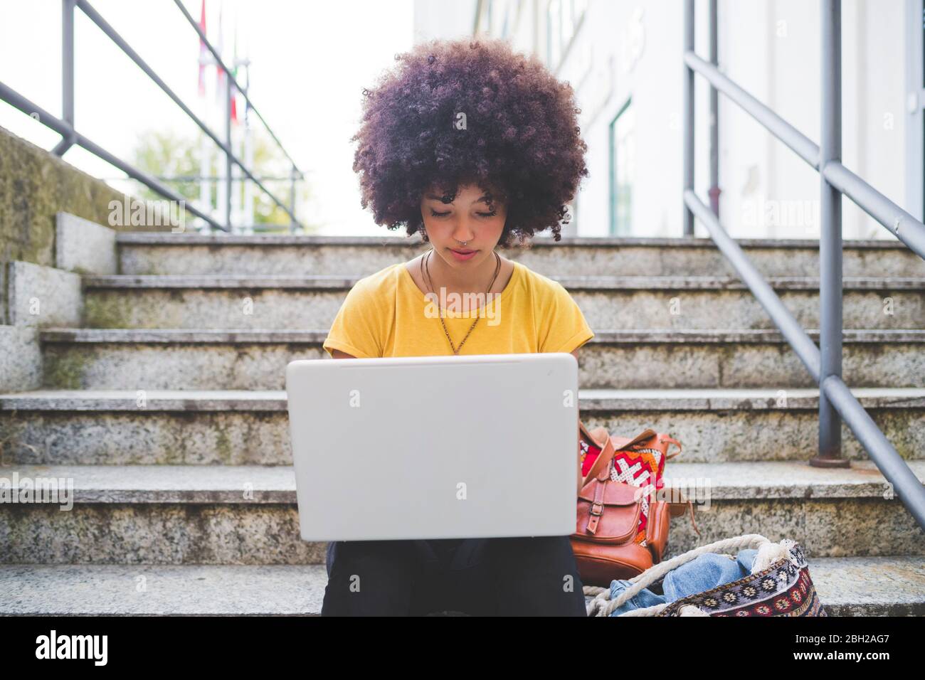 Junge Frau mit Afro-Frisur mit Laptop auf Treppen in der Stadt Stockfoto