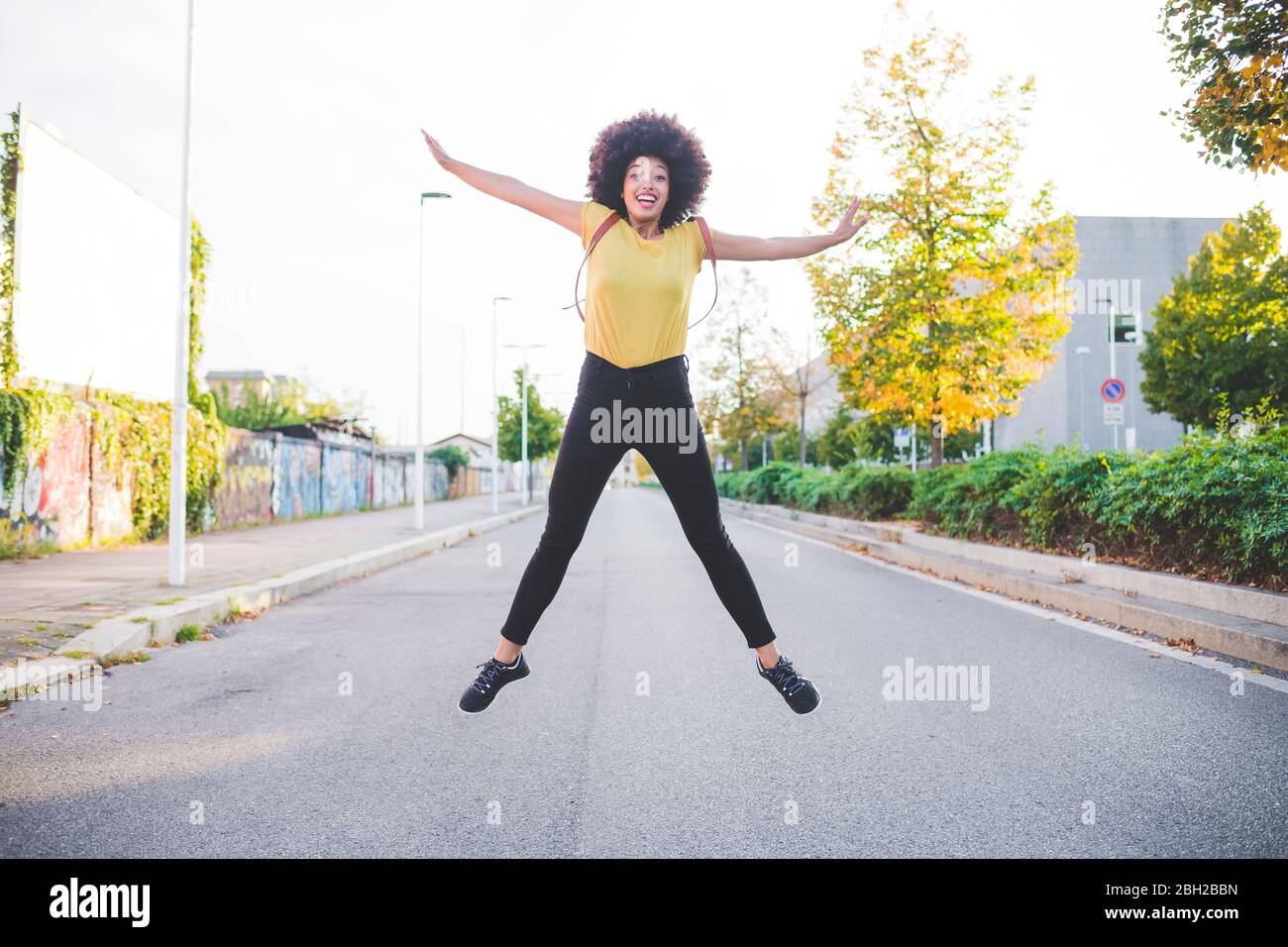 Glückliche junge Frau mit afro Frisur Springen auf einer Straße in der Stadt Stockfoto
