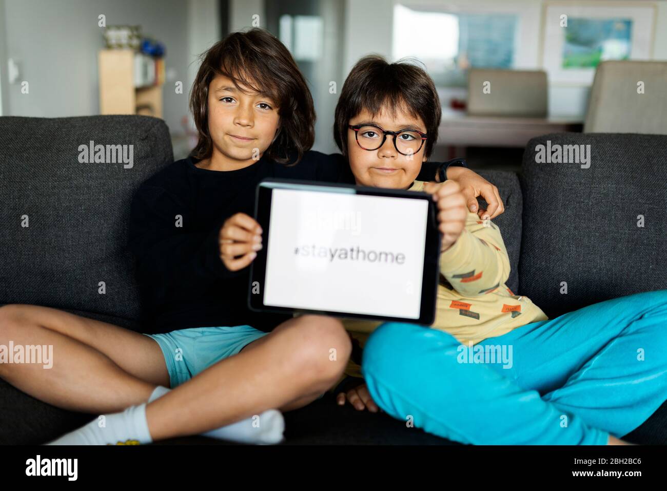 Portrait von zwei Brüdern sitzen auf Couch zu Hause präsentiert digitale Tablet mit Anfrage Stockfoto