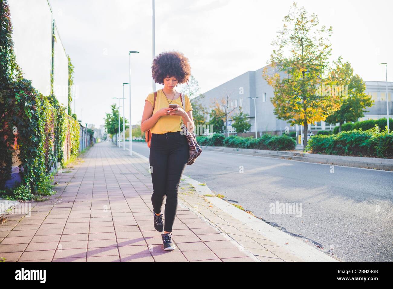 Junge Frau mit Afro-Frisur mit Smartphone in der Stadt Stockfoto