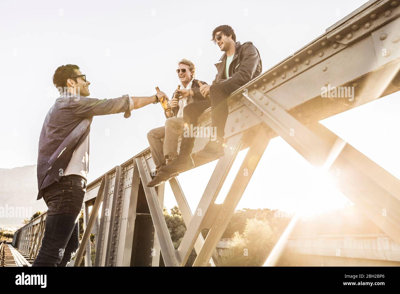 Drei Männer trinken Bier auf einer alten Eisenbahnbrücke Stockfoto