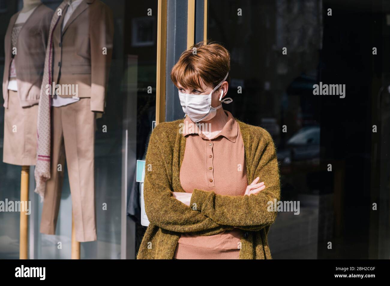 Frau in Maske vor ihrem geschlossenen Bekleidungsgeschäft stehend Stockfoto