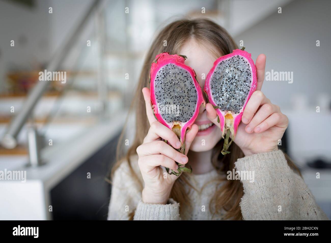 Lachendes Mädchen, das die Augen mit zwei Hälften der Drachenfrucht bedeckt Stockfoto