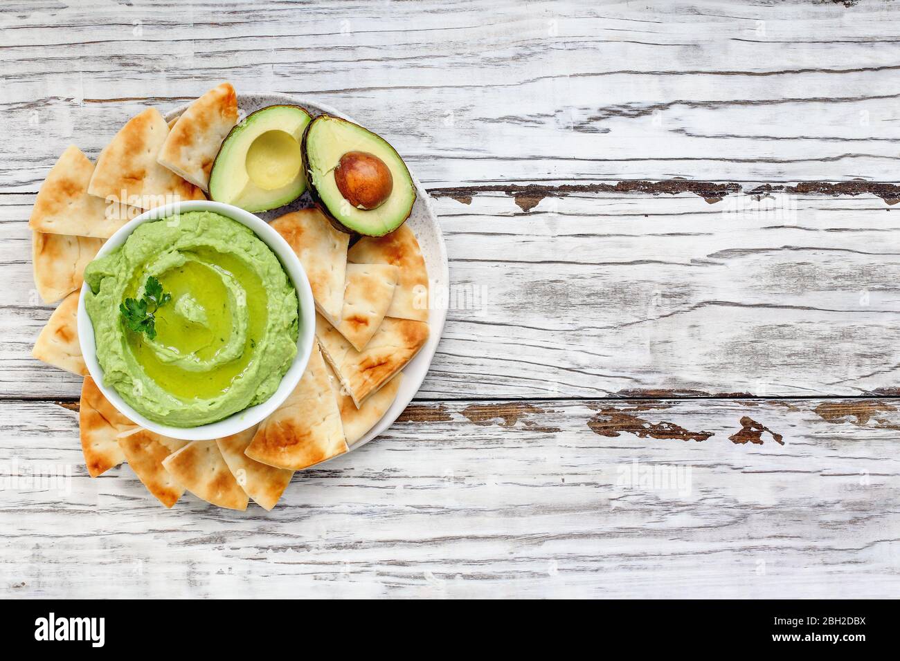 Draufsicht auf Avocado Hummus, hergestellt mit Kichererbsen, Avocados und Tahini, mit Olivenöl. Garniert mit Petersilie und serviert mit Pita Brot über einem rustikalen Stockfoto