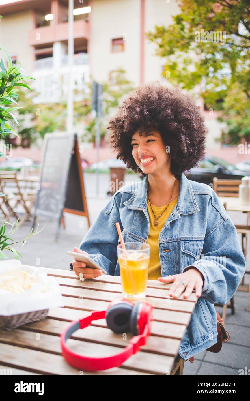 Glückliche junge Frau mit Afro-Frisur in einem Café im Freien in der Stadt Stockfoto
