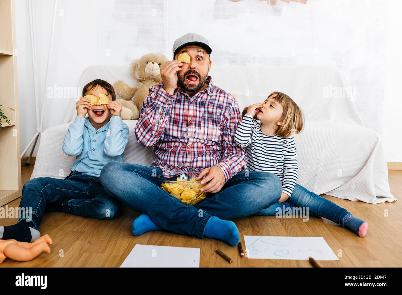 Fahther und Kinder sitzen auf dem Boden und bedecken die Augen mit Kartoffelchips Stockfoto