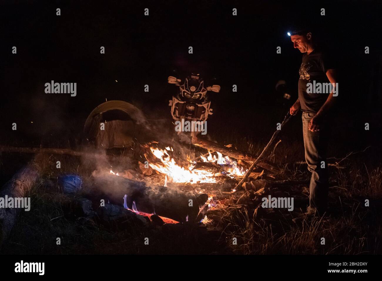 Mann auf einem Motorradausflug in der Nacht am Lagerfeuer Stockfoto