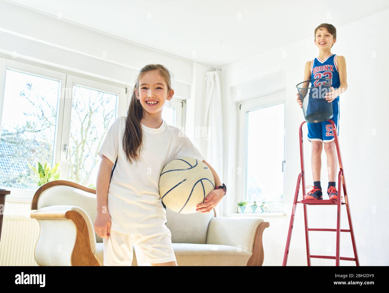 Portrait von Mädchen und Jungen Basketball spielen im Wohnzimmer Stockfoto