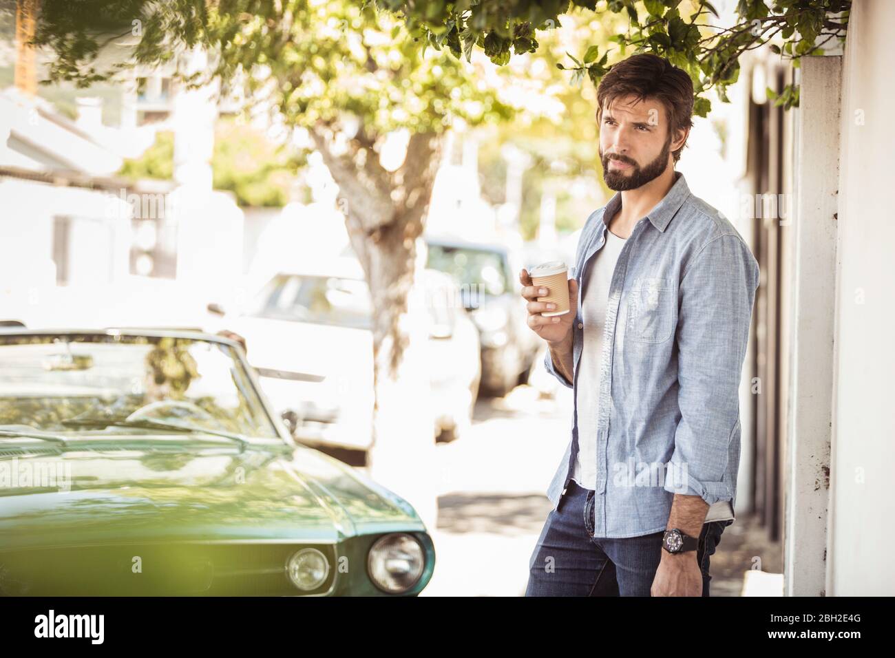 Mann hält Kaffee zum Mitnehmen neben dem Cabrio Stockfoto