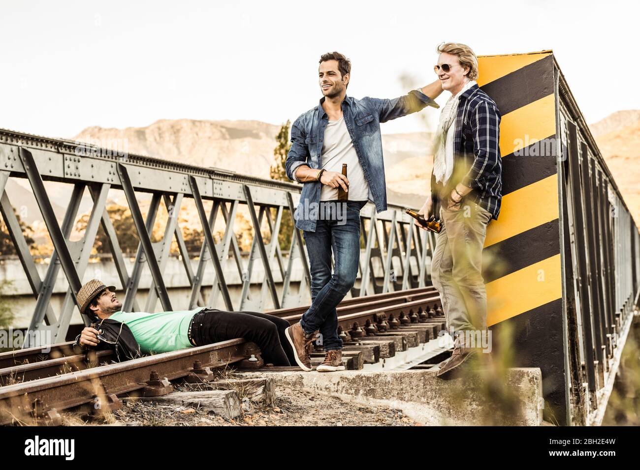 Drei Männer trinken Bier auf einer alten Eisenbahnbrücke Stockfoto