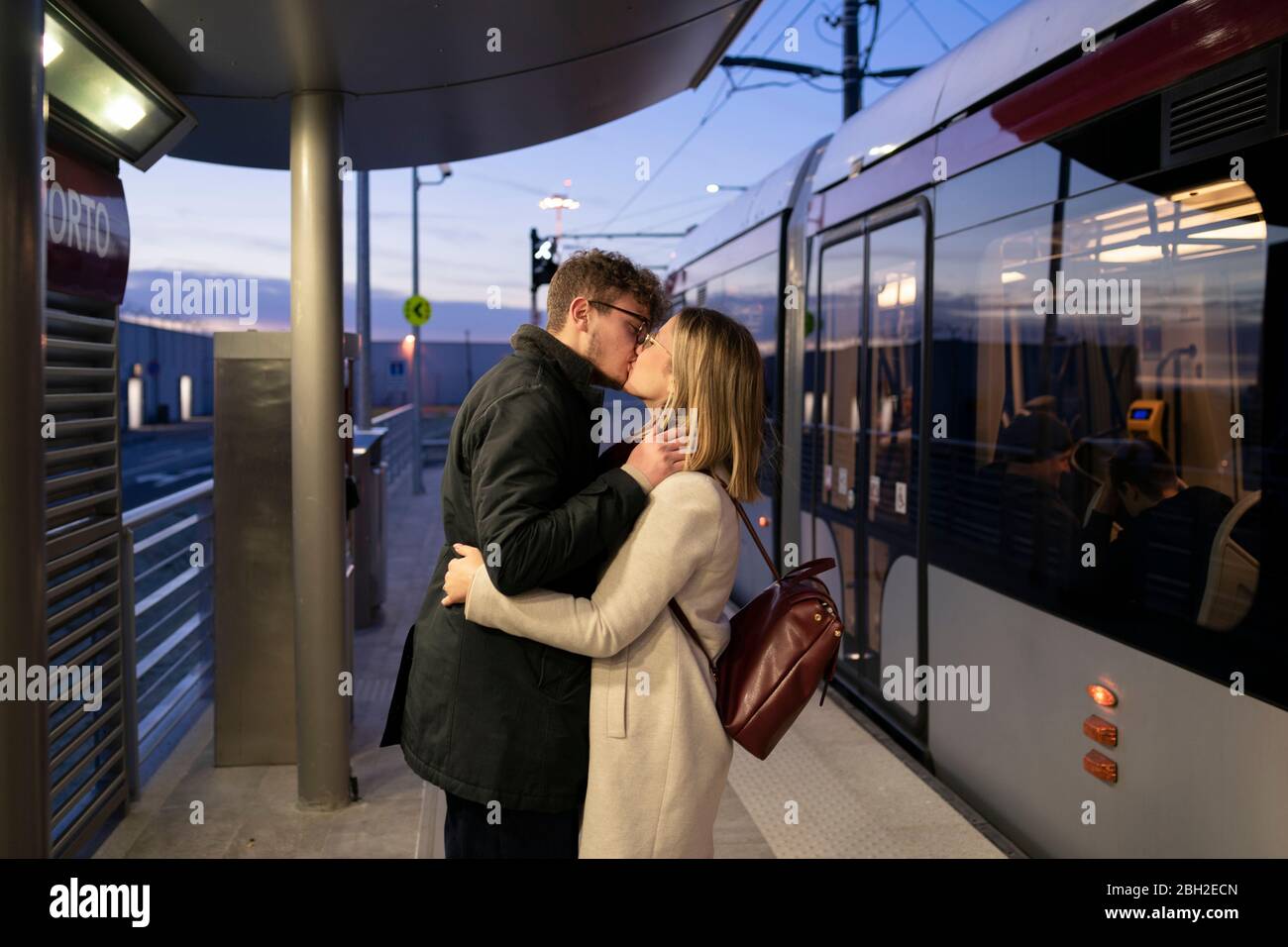 Küssen junges Paar an der Straßenbahnhaltestelle am Abend stehen Stockfoto