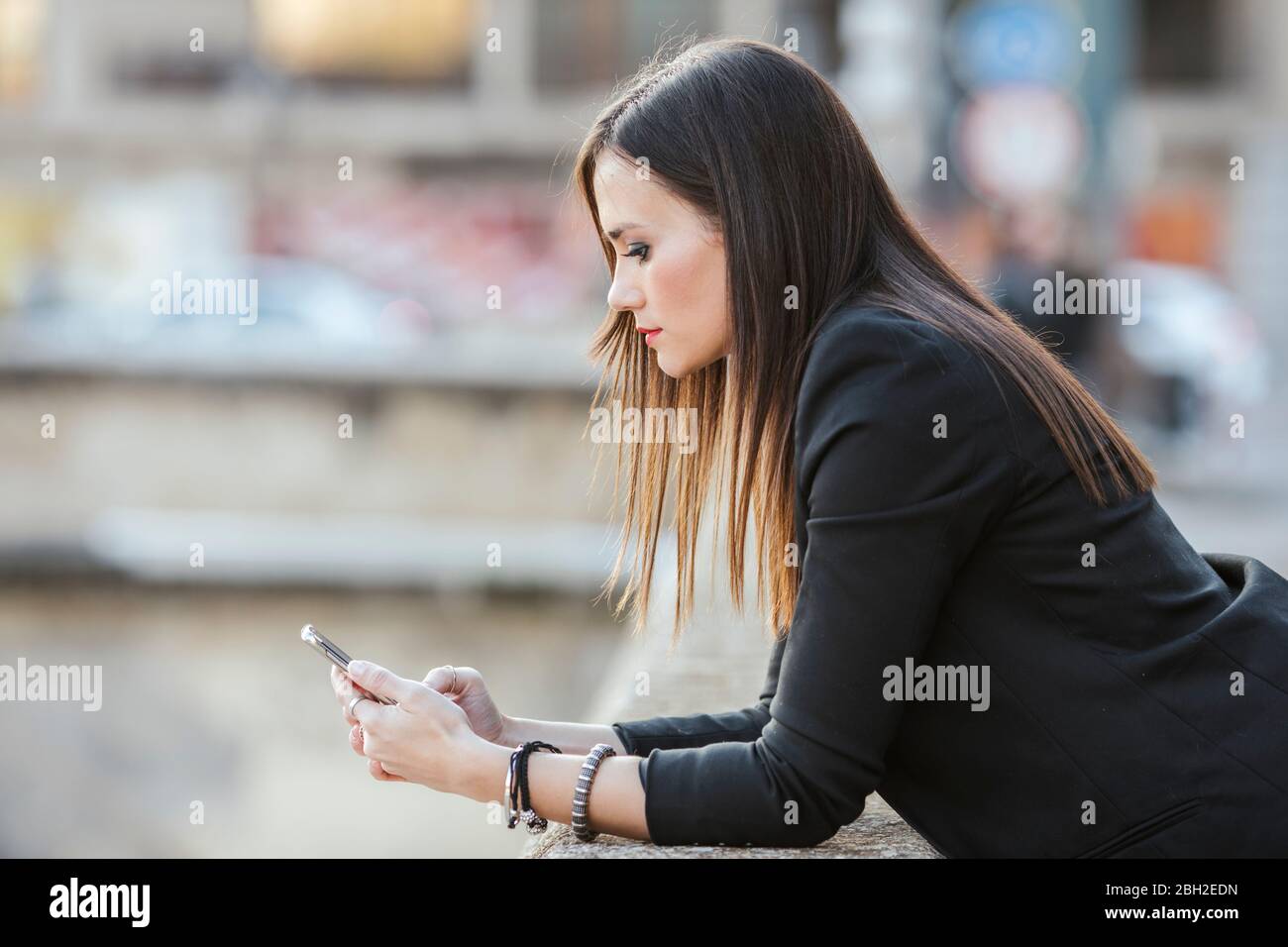 Seriöse Frau, die sich an einer Wand lehnt und auf das Mobiltelefon schaut Stockfoto