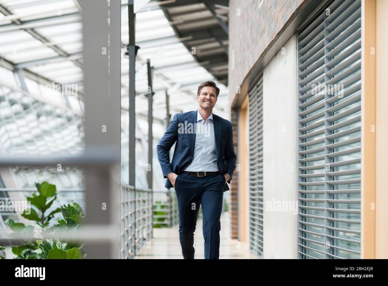 Selbstbewusster Geschäftsmann, der auf der Galerie des grünen Atriums läuft Stockfoto