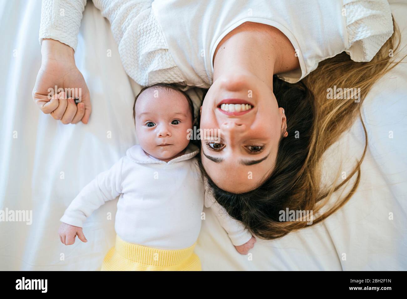 Mutter und Baby liegen im Bett und blicken auf die Kamera Stockfoto
