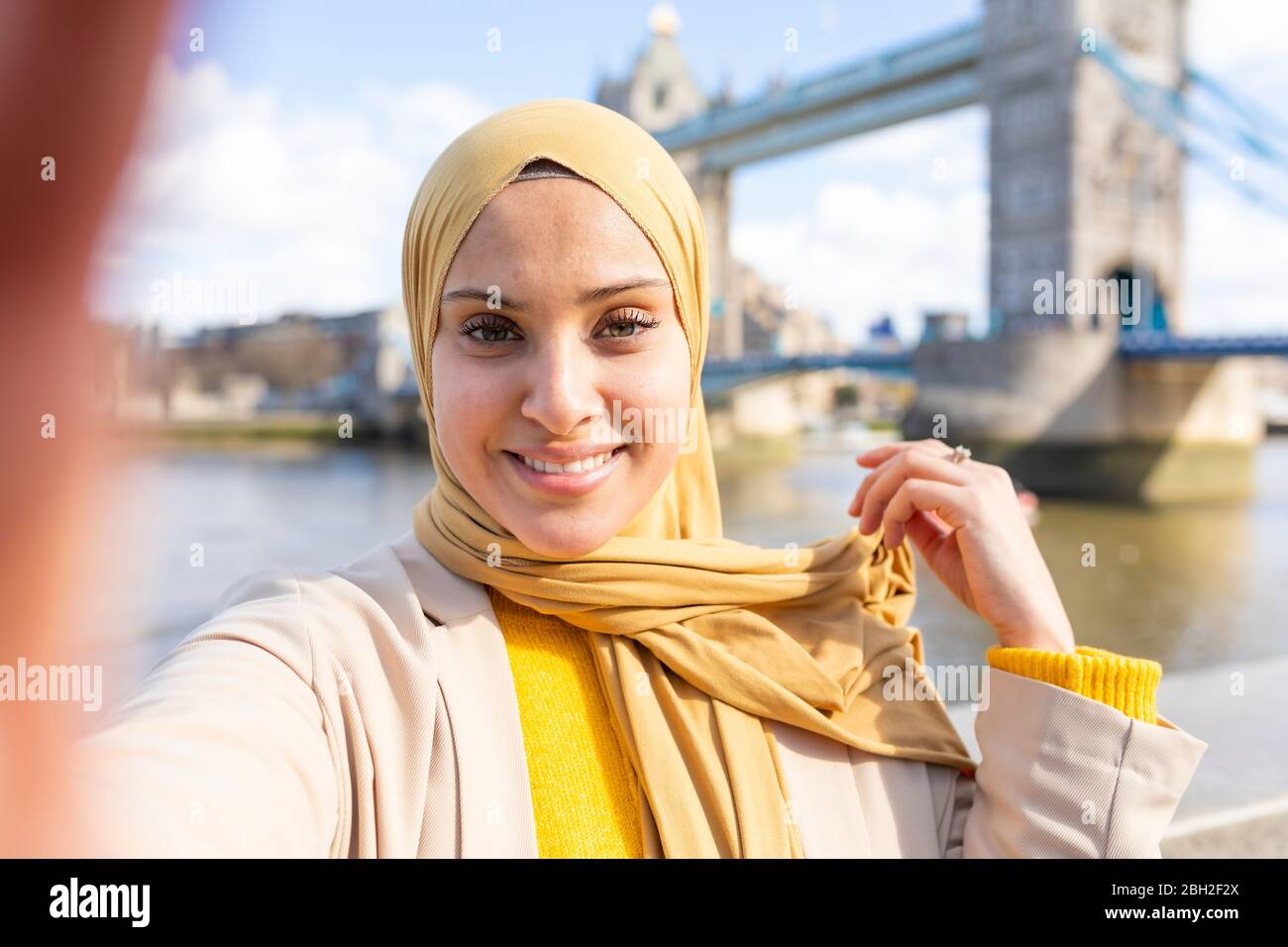 Porträt einer lächelnden jungen Frau, die vor der Tower Bridge ein Selfie macht, London, Großbritannien Stockfoto