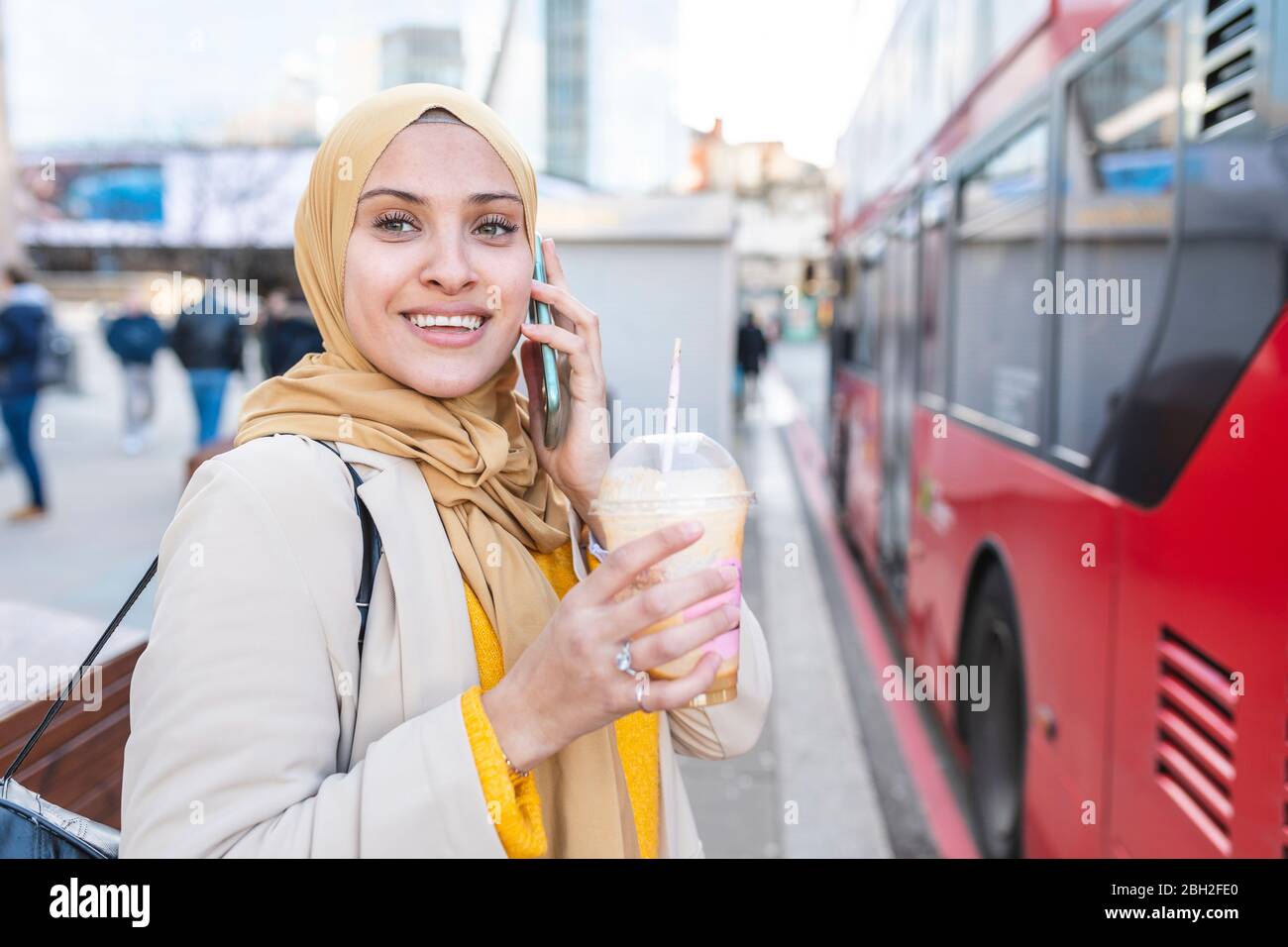 Porträt einer lächelnden jungen Frau am Telefon an der Bushaltestelle warten Stockfoto