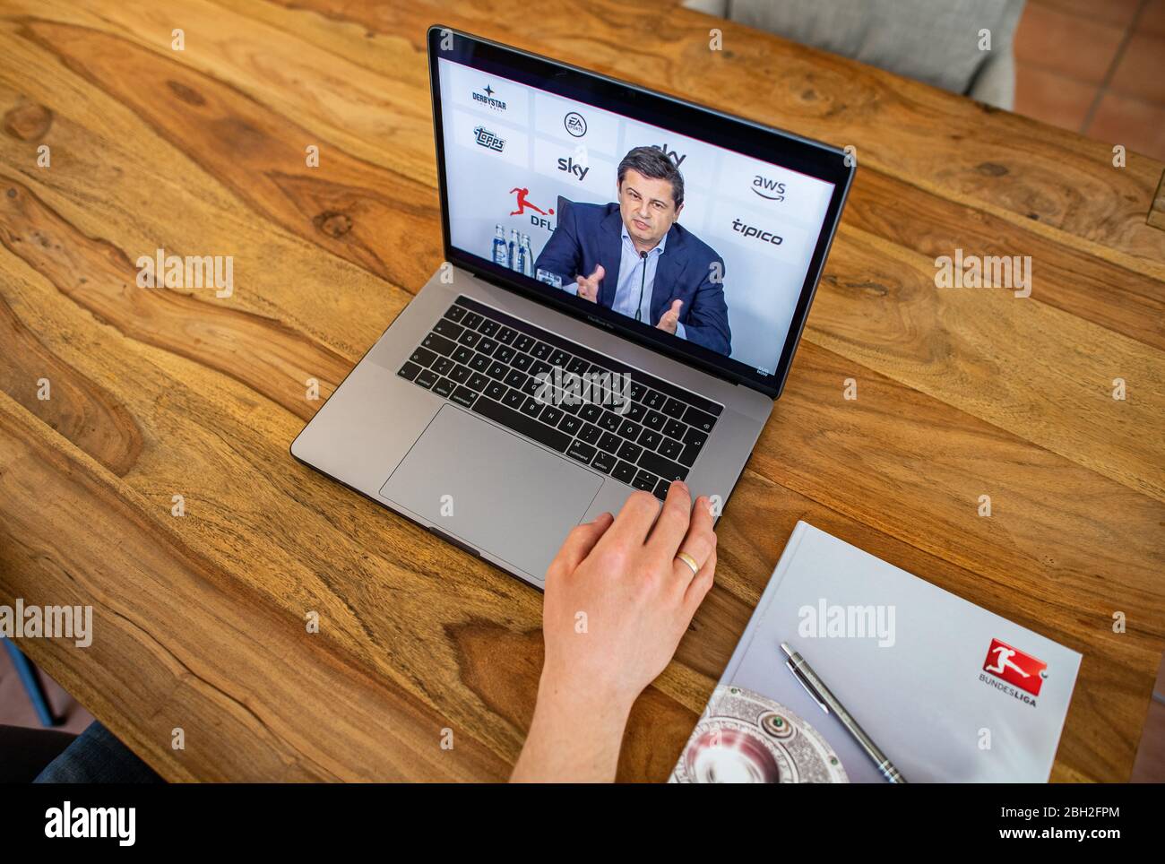 Warendorf, Deutschland. April 2020. Ein Mann schaut auf den Monitor seines Laptops, auf dem Christian Seifert, CEO und Sprecher des Vorstands der Deutschen Fußball-Liga (DFL), während einer Live-Video-Pressekonferenz nach der DFL-Hauptversammlung zu den Folgen der Corona-Pandemie zu sehen ist. Kredit: Guido Kirchner/dpa/Alamy Live News Stockfoto