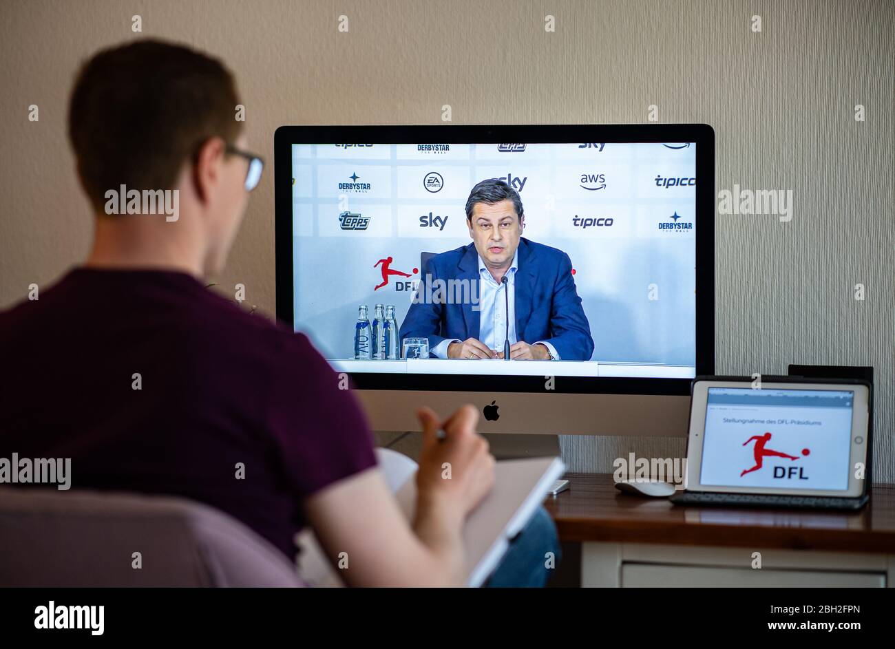 Warendorf, Deutschland. April 2020. Ein Mann schaut auf den Monitor seines Computers, auf dem Christian Seifert, CEO und Sprecher des Vorstands der Deutschen Fußball-Liga (DFL), während einer Live-Video-Pressekonferenz nach der DFL-Hauptversammlung zu den Folgen der Corona-Pandemie zu sehen ist. Kredit: Guido Kirchner/dpa/Alamy Live News Stockfoto