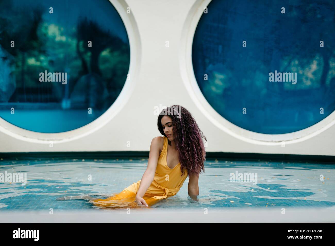Junge Frau in gelbem Sommerkleid im Pool sitzen Stockfoto
