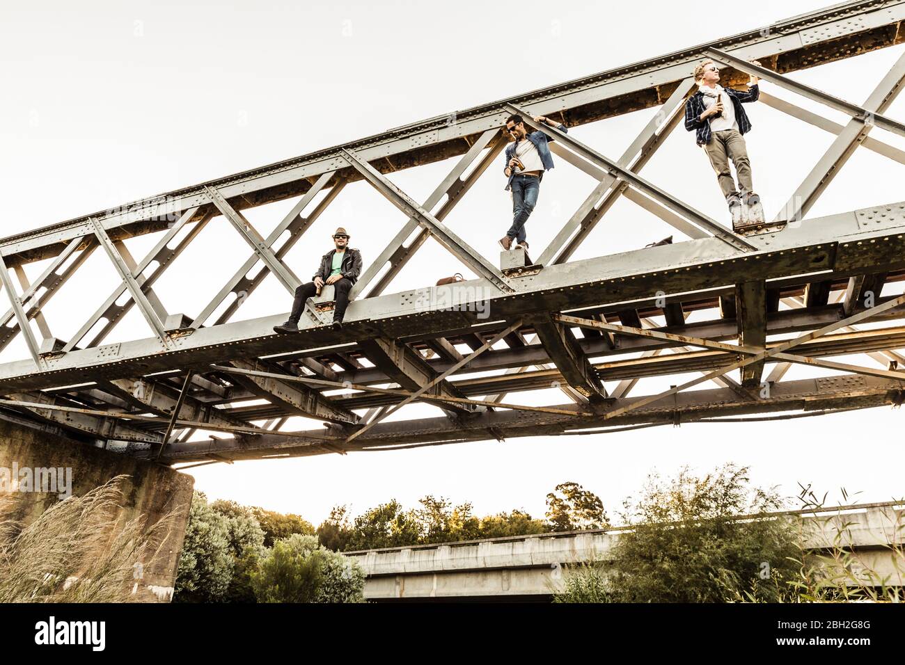 Drei Männer mit Bierflaschen auf einer alten Eisenbahnbrücke Stockfoto