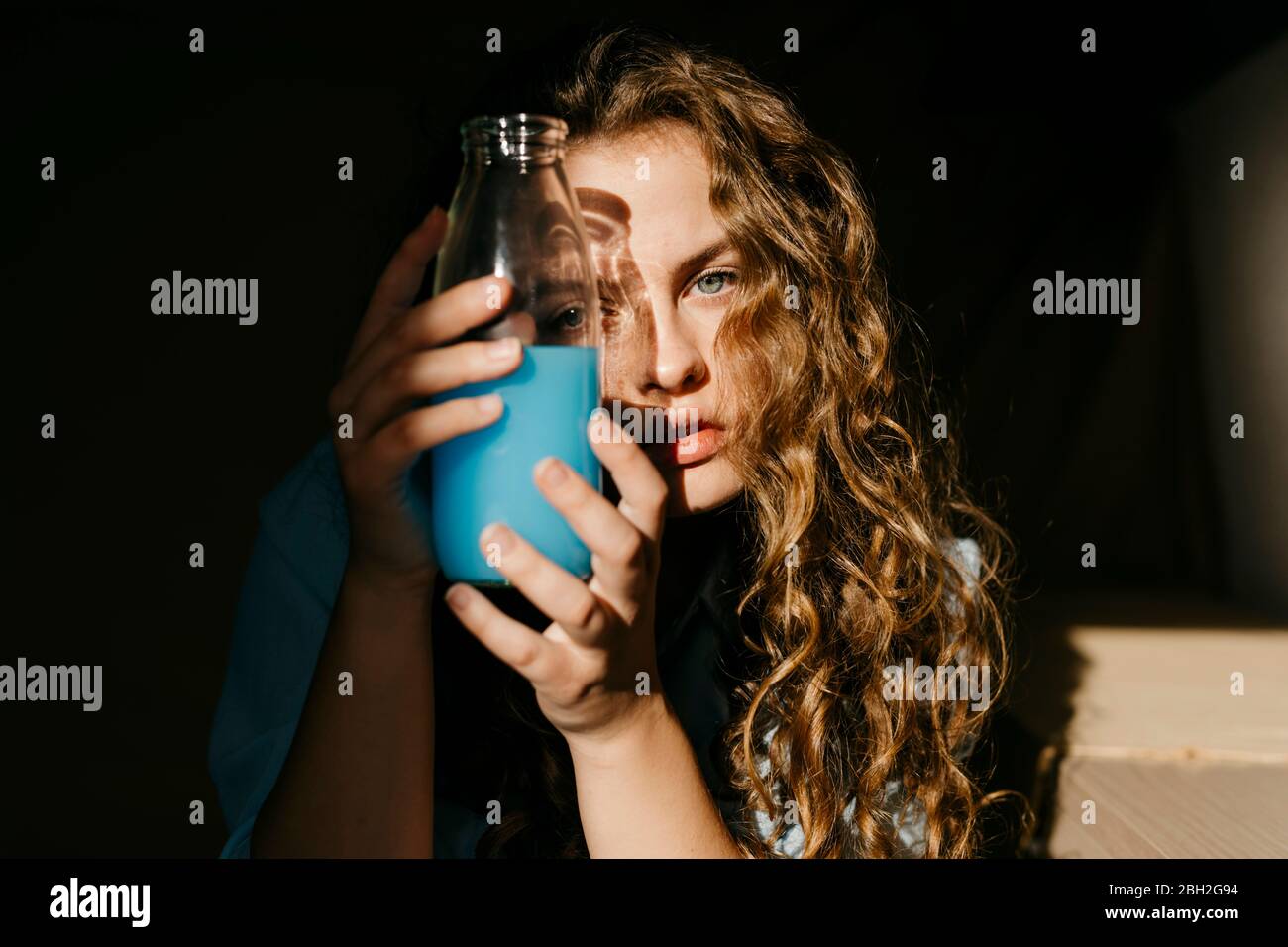 Portrait der blonden jungen Frau zu Hause hält farbige Flasche Stockfoto