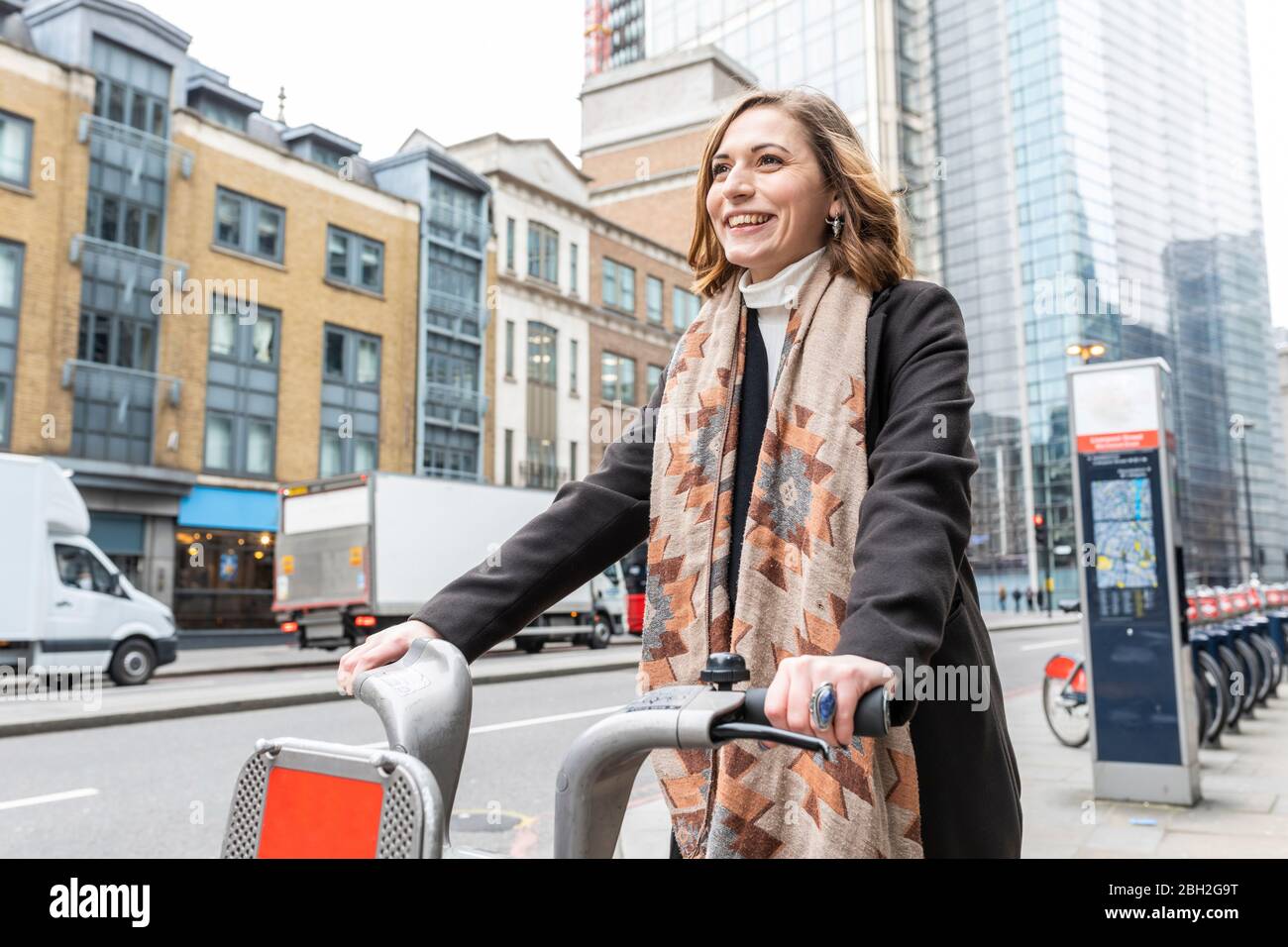Glückliche Frau in der Stadt mit Leihrad, London, Großbritannien Stockfoto