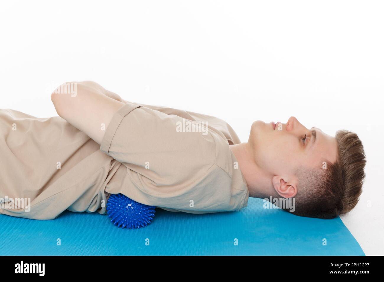 Schöner Mann zeigt Übungen mit dem Ball mit Spikes für eine myofascial Release Massage von Triggerpunkten. Massage der Wirbelsäulenmuskulatur. Isoliert auf w Stockfoto