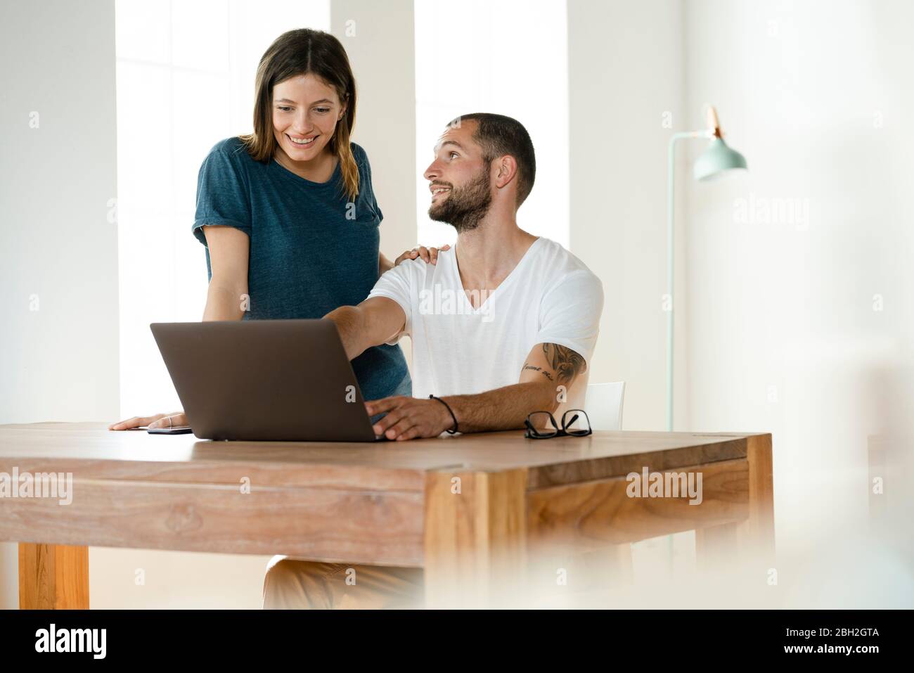 Lächelndes Paar, das von zu Hause aus im modernen Wohnzimmer am Laptop arbeitet Stockfoto