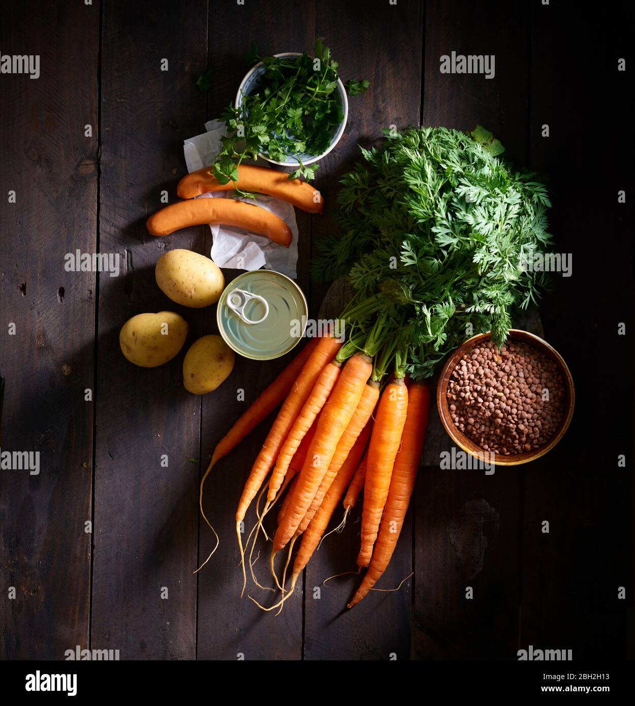 Ein Bündel Karotten, Würstchen, Petersilie, Kartoffeln, Linsensuppe aus der Dose und eine Schüssel Linsen Stockfoto