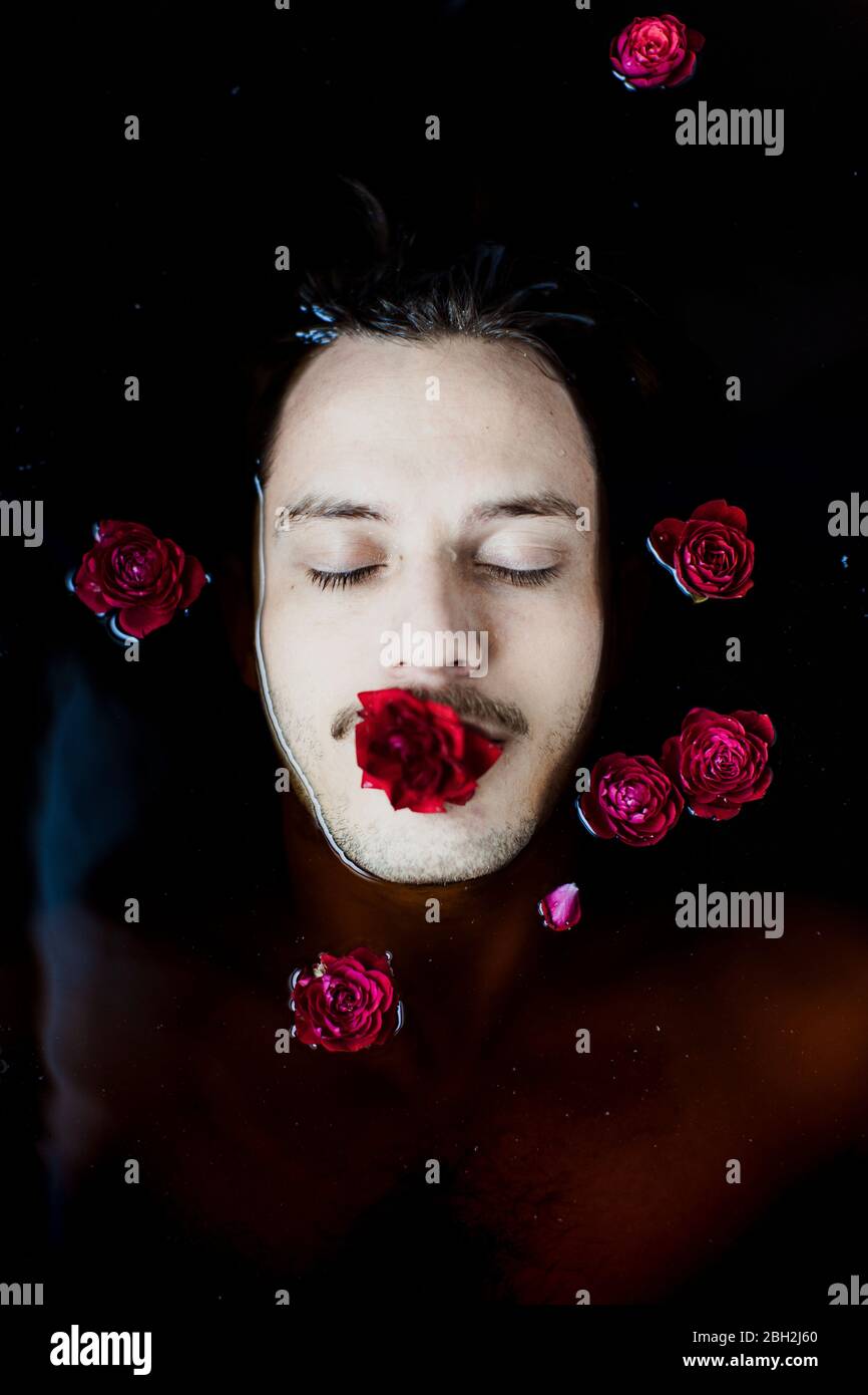 Porträt eines jungen Mannes mit roter Rose im Mund im Wasser schweben Stockfoto